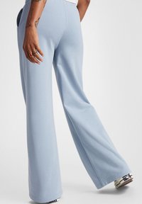 Pantalones de pierna ancha de color azul claro, hechos de una tela suave, con cinturilla elástica y bolsillos laterales. Textura suave con un ajuste relajado.