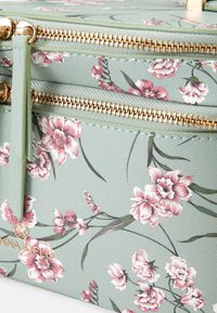 Mintgroene tas met een bloemenpatroon en twee gouden ritsen, versierd met roze bloemen en groene bladeren tegen een gestructureerde achtergrond.