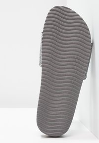 Grey rubber sandal sole featuring a wavy textured pattern, with a black printed strap providing additional support and contrast.