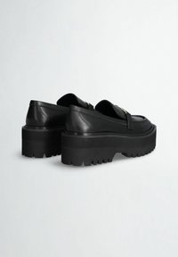 Scarpe platform in pelle nera con suola spessa, caratterizzate da una punta arrotondata e una fascia decorativa. Suola in gomma texturizzata per una buona aderenza.