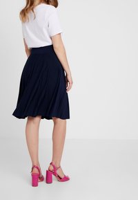 Falda de vuelo azul marino con cintura alta, combinada con sandalias de tacón rosas con textura de cocodrilo. Diseñada para un look casual.
