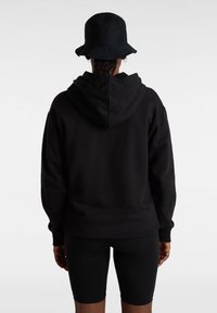 Sudadera con capucha negra de corte relajado, hecha de material suave. Combinada con pantalones cortos de ciclismo negros, que presentan un diseño minimalista.