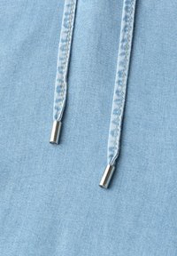 Gros plan d’un tissu bleu clair avec deux cordons cousus se terminant par des embouts métalliques argentés.