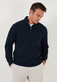 Navy blue pullover sweater with a textured ribbed pattern, features a half-zip collar and long sleeves, made of soft fabric.