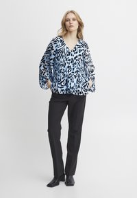 Blusa a maniche lunghe blu e nera con un motivo, scollo a V, abbinata a pantaloni slim-fit neri e stivaletti. Tessuto con texture liscia.