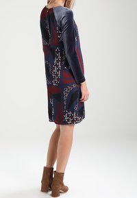 Langärmliges Kleid mit einem marineblauen und burgunderfarbenen Muster und geometrischen Designs, gefertigt aus einem glatten Stoff. Mit einem Samtkragen akzentuiert.