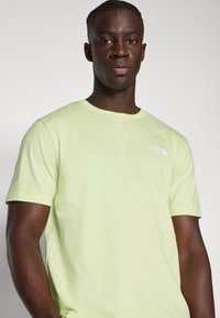 Limegrünes T-Shirt aus weichem Stoff, mit Rundhalsausschnitt und kurzen Ärmeln. Zeigt ein kleines weißes Logo auf der linken Brustseite.