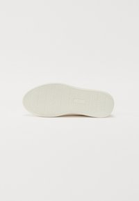 Hvit sneakersåle med teksturert gripe mønster og liten rektangulær merkevarelogo i midten, vist flatt på en hvit bakgrunn.