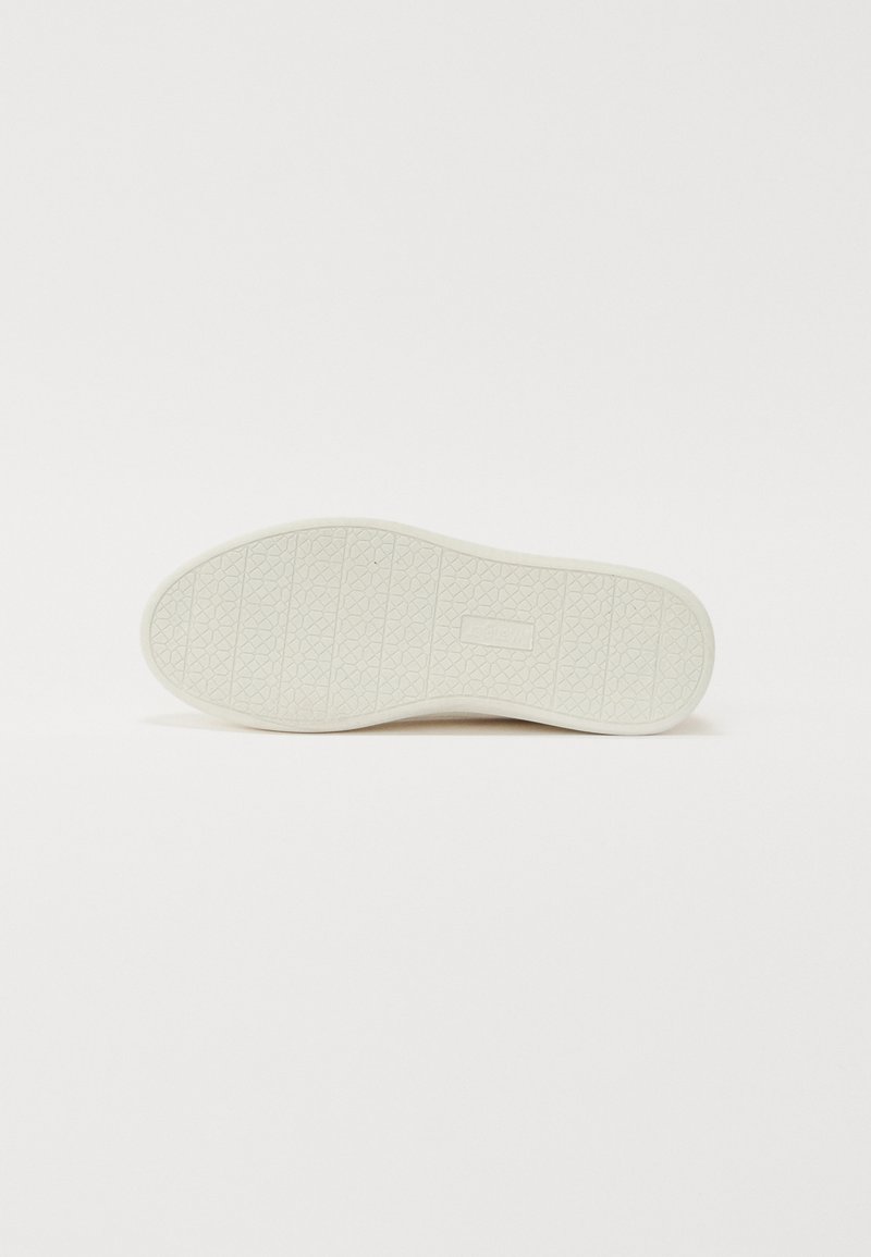 Suela de zapatilla blanca con patrón de agarre texturizado y pequeño logotipo rectangular de la marca en el centro, presentada plana sobre un fondo blanco.