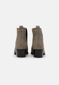 Stivaletti alla caviglia in suede taupe con tacco basso a blocco, caratterizzati da borchie decorative lungo i lati e un'etichetta per facilitarne l'indossamento.
