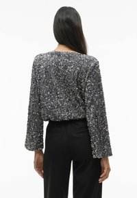 Glitterend grijs pailletten top met lange mouwen, ronde hals en een losse pasvorm; gestyled met zwarte broek, waarbij textuur en versieringen worden getoond.