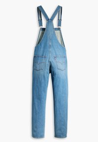 Salopette en denim bleu clair avec bretelles réglables, deux poches avant et deux poches arrière arborant un logo de marque.