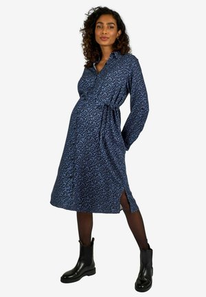 Abito premaman blu navy con stampa leopardata, vita con cintura, maniche lunghe, apertura frontale con bottoni e spacchi laterali. Abbinato a stivaletti neri.