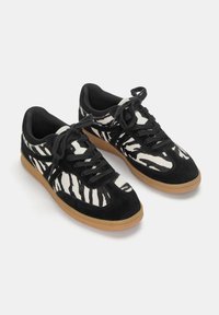 Sneaker con stampa zebra in bianco e nero, realizzati in materiali scamosciati e tessili, con lacci tondi e suola in gomma beige.