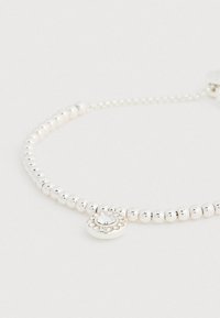 Sidabrinė apyrankė su karoliukais, turinti centriniame rate žydintį skaidrų akmenį, apsuptą mažesniais brangakmeniais. Lygi tekstūra, reguliuojamas ilgis.