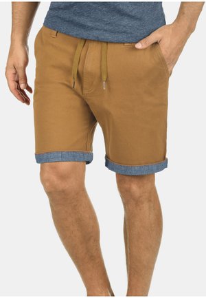 Pantalones cortos de hombre en algodón color beige con puños de denim enrollados, que cuentan con una cintura con cordón y bolsillos laterales. Textura suave y ajuste casual.
