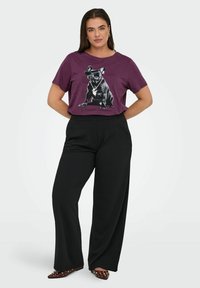 Lilla bomuld T-shirt med en sort-hvid grafik af en hund iført solbriller, kombineret med løse sorte bukser og spidse bordeauxsko.