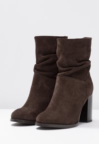 Botas de tobillo de ante marrón con un diseño arrugado y un tacón ancho, con punta redondeada y textura suave.