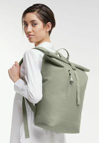 Zielony plecak z rolowanym zamknięciem, z regulowanymi ramiączkami, wykonany z gładkiego, trwałego materiału. Posiada przednią kieszeń na zamek i minimalistyczny design.