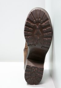 Brązowa gumowa podeszwa buta z teksturowanym bieżnikiem zapewniającym przyczepność. Posiada solidny, szeroki obcas oraz wyraźny wzór w diamenty dla stabilności.
