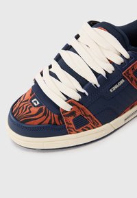 Navy blue and burnt orange sneaker with black tiger stripes, thick white laces, and "Globe" branding on side and sole.