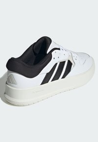 Sneaker bianco con dettagli neri e tre strisce, materiale in pelle liscia, punta rotonda, collo imbottito e suola testurizzata.