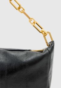 Svart läderhandväska med texturerad yta, utrustad med en guldkedja som kopplas till toppen och framhäver geometriska former.