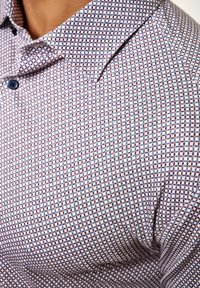 Kurzarmhemd aus leichtem Stoff mit einem geometrischen Muster in Blau, Maroon und Weiß. Mit einem spitzen Kragen und Knopfverschluss.