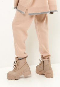 Botas de tobillo beige con una plataforma gruesa, cuello forrado de piel y parte delantera con cordones. Combinadas con pantalones de chándal tapered en rosa claro.