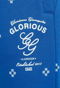 Królewsko niebieska bluza z białym napisem "Glorious Gangsta" oraz "London Established 2013", ozdobiona wzorzystymi akcentami na całej powierzchni.