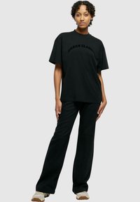 T-shirt en coton noir à manches courtes et col rond, avec le texte "URBAN CLASSIC" sur la poitrine. Associé à un pantalon large noir assorti.