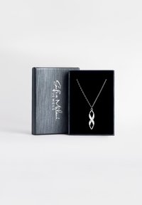 Silverhalsband med en oändlighetssymbol hänge, prydd med små klara stenar, visad i en texturerad mörkgrå smyckeslåda.