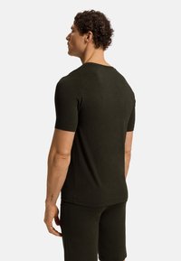 Tmavě zelené tričko s krátkým rukávem, přiléhavý střih, měkká textura, kulatý výstřih. Nosené s odpovídajícími kraťasy, s minimálními švy.