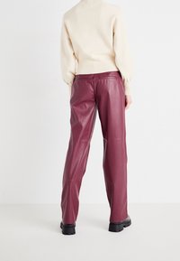Pantalons en cuir bordeaux avec une coupe droite, texture lisse et poches arrière. Associés à un pull en tricot couleur crème.