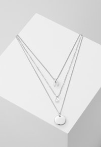 Trys sidabriniai kaklo papuošalai skirtingų ilgių. Viršutinė grandinė turi norų kauliuko pakabuką, vidurinė - ašaros formos žavesį, o apatiniame - apvalų pakabuką.