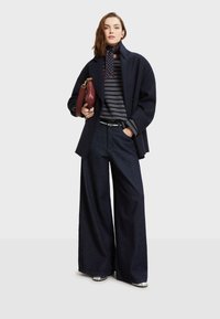 Námornícky kabát cez šedý pruhovaný rolák, skombinovaný s širokými tmavými džínsami. Doplnky tvoria bordová kabelka a vzorovaný šál.