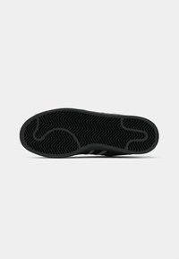 Black sneaker sole with a textured rubber finish, featuring a zigzag pattern and a rounded toe design. Three white stripes accent the side.