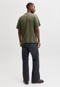 Olivengrøn kortærmet T-shirt med en afslappet pasform, kombineret med mørkegrå jeans og brune sko, set bagfra.