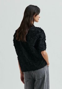 Maglietta nera con ricamo floreale testurizzato, maniche corte, vestibilità rilassata, indossata con jeans grigi a vita alta.