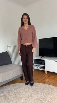 Casaco de malha cor-de-rosa com botões, combinado com calças largas cor de vinho. Sapatos pretos de fácil calçar. Tecido simples e texturizado, design cropped.