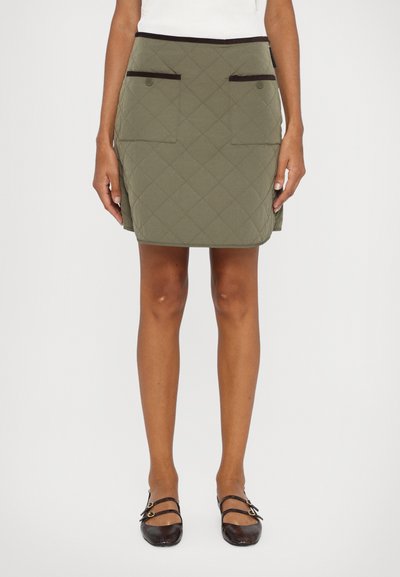 Khaki quilted skirt with two front pockets, dark trim along the waistband, and a straight silhouette. Worn with black flats.