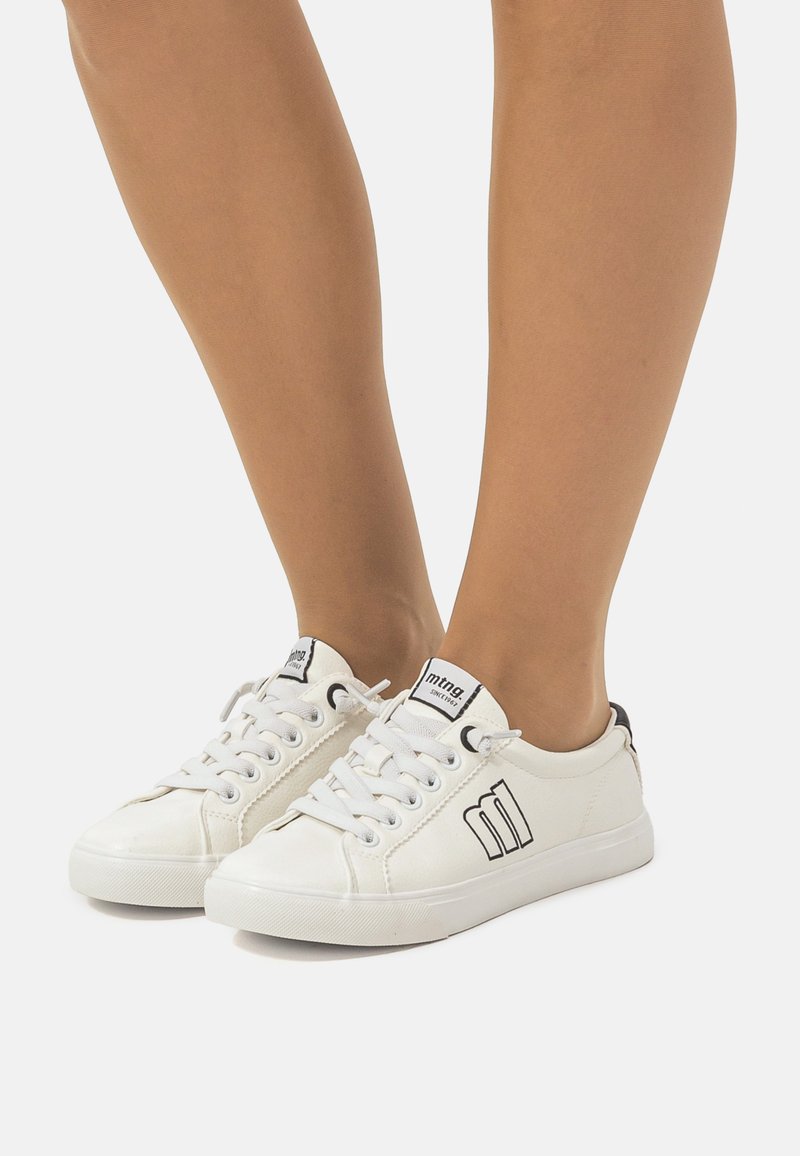 Zapatillas blancas con acentos y logotipo en negro. Material de cuero suave, puntera redonda, suela plana y diseño de cordones. Construcción duradera.