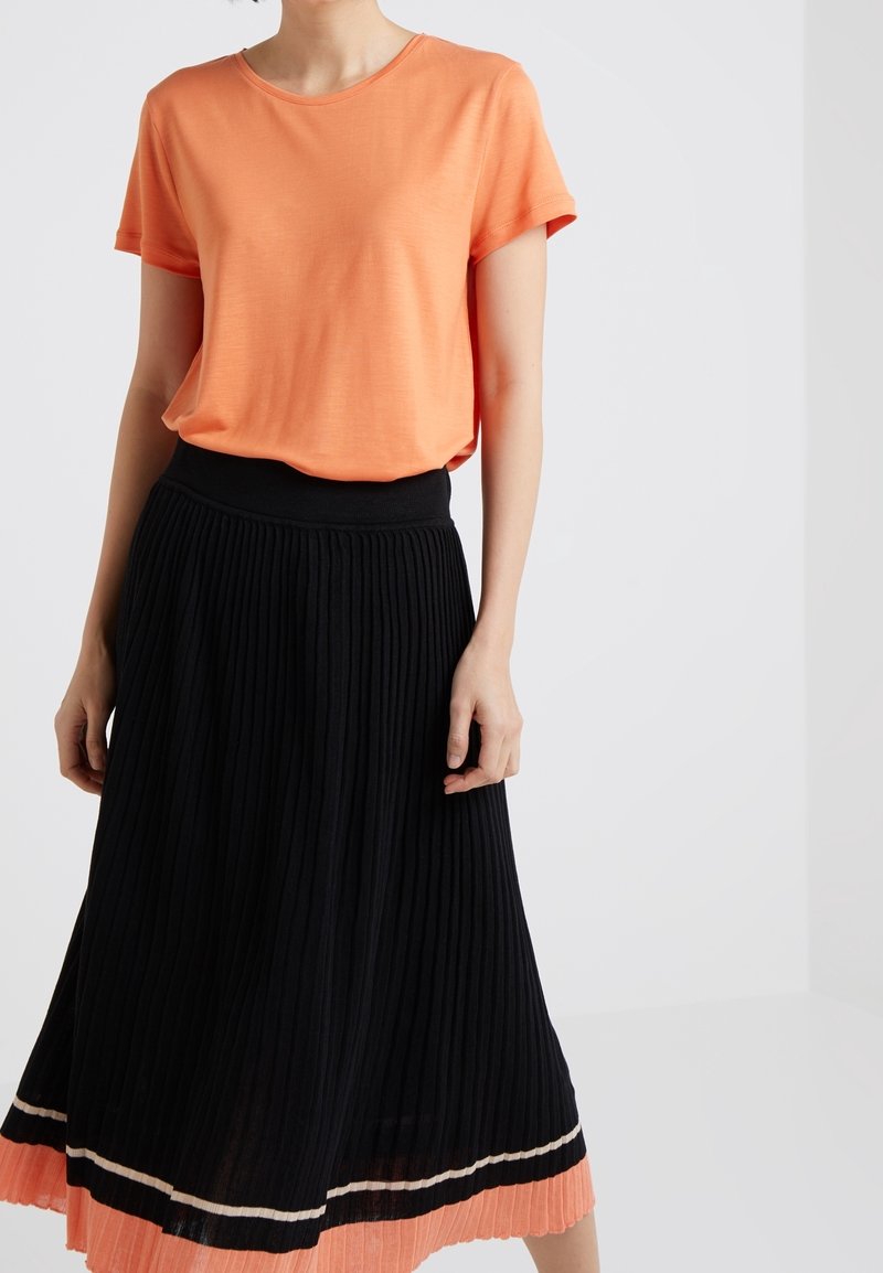 Orange t-shirt med kort ärm i kombination med en svart plisserad kjol som har en färgblockerad nederkant i korall och kräm med horisontella ränder.