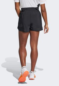 Shorts de sport noirs avec une taille à cordon de serrage, des accents réfléchissants légers et une texture lisse et légère. Associés à des chaussures blanches et orange.