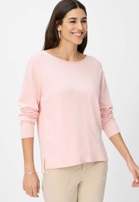 Lichtroze longsleeve top met een relaxte pasvorm, ronde halslijn en zijsplitten. Zacht, glad materiaal met minimale stikdetails.