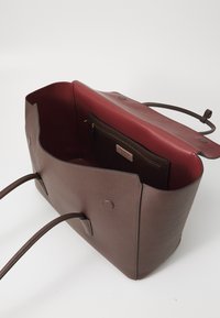 Sac fourre-tout en cuir marron avec un extérieur texturé et un intérieur lisse maroon. Doté de longues poignées et d'un compartiment zippé.