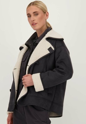 Veste en shearling noir avec un col et des poignets crème, design à double boutonnage, accents de boutons à l'avant et coupe cropped.