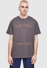 Szara bawełniana koszulka z krótkim rękawem, z wyblakłym nadrukiem graficznym przedstawiającym wykonawcę oraz napisem "THE SHOW" w kolorze rdzy.