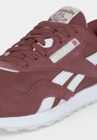 Κόκκινο-βυσσινί και λευκό παπούτσι Reebok με υφές από σουέντ και ύφασμα, με λογότυπο Reebok και βρετανική σημαία στην πλευρική επιφάνεια.