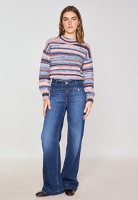 Maglione a righe in tonalità pastello con scollo rotondo, abbinato a jeans in denim blu a vita alta e gamba larga con tasche frontali e bottoni.